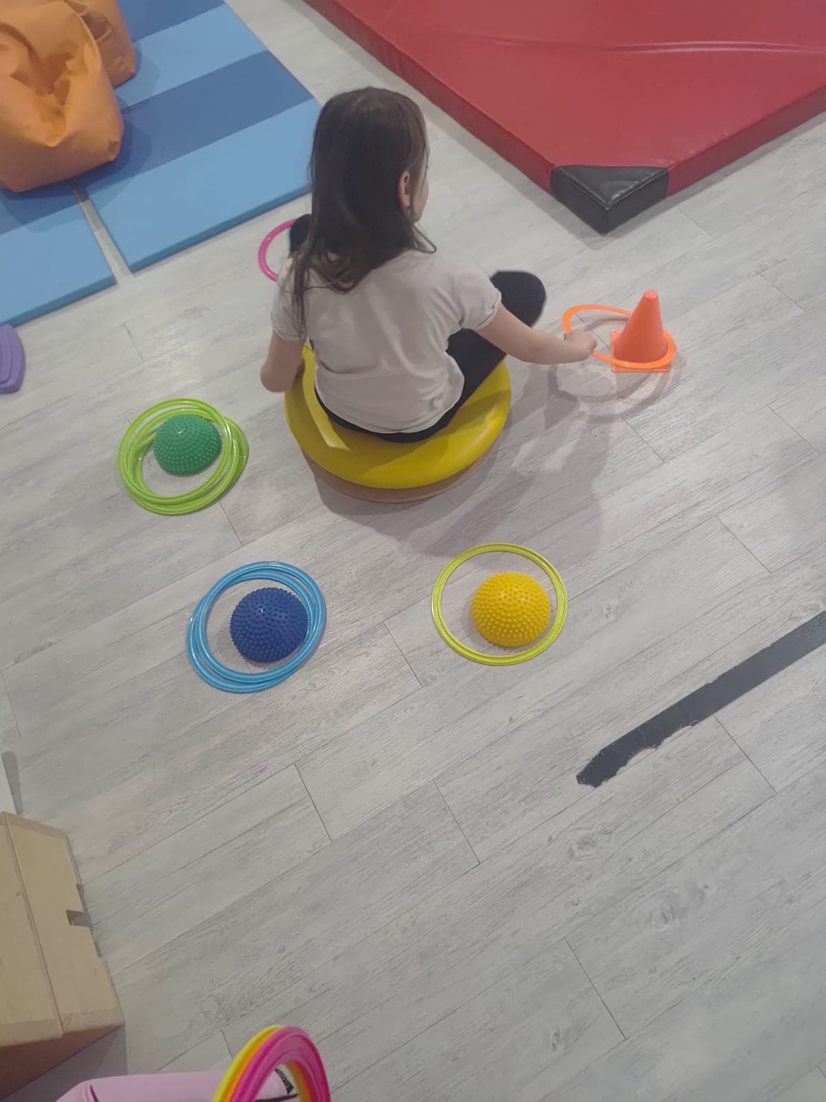 Dziecko wykonuje ćwiczenie równoważne z wykorzystaniem pomocy terapeutycznych.