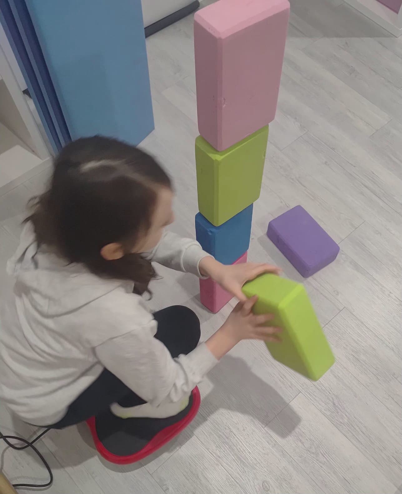 Dziecko wykonuje ćwiczenie na platformie wibracyjnej podczas terapii.