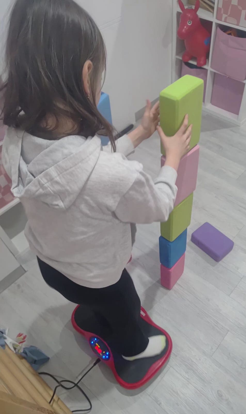 Dziecko wykonuje ćwiczenie na platformie wibracyjnej podczas terapii.